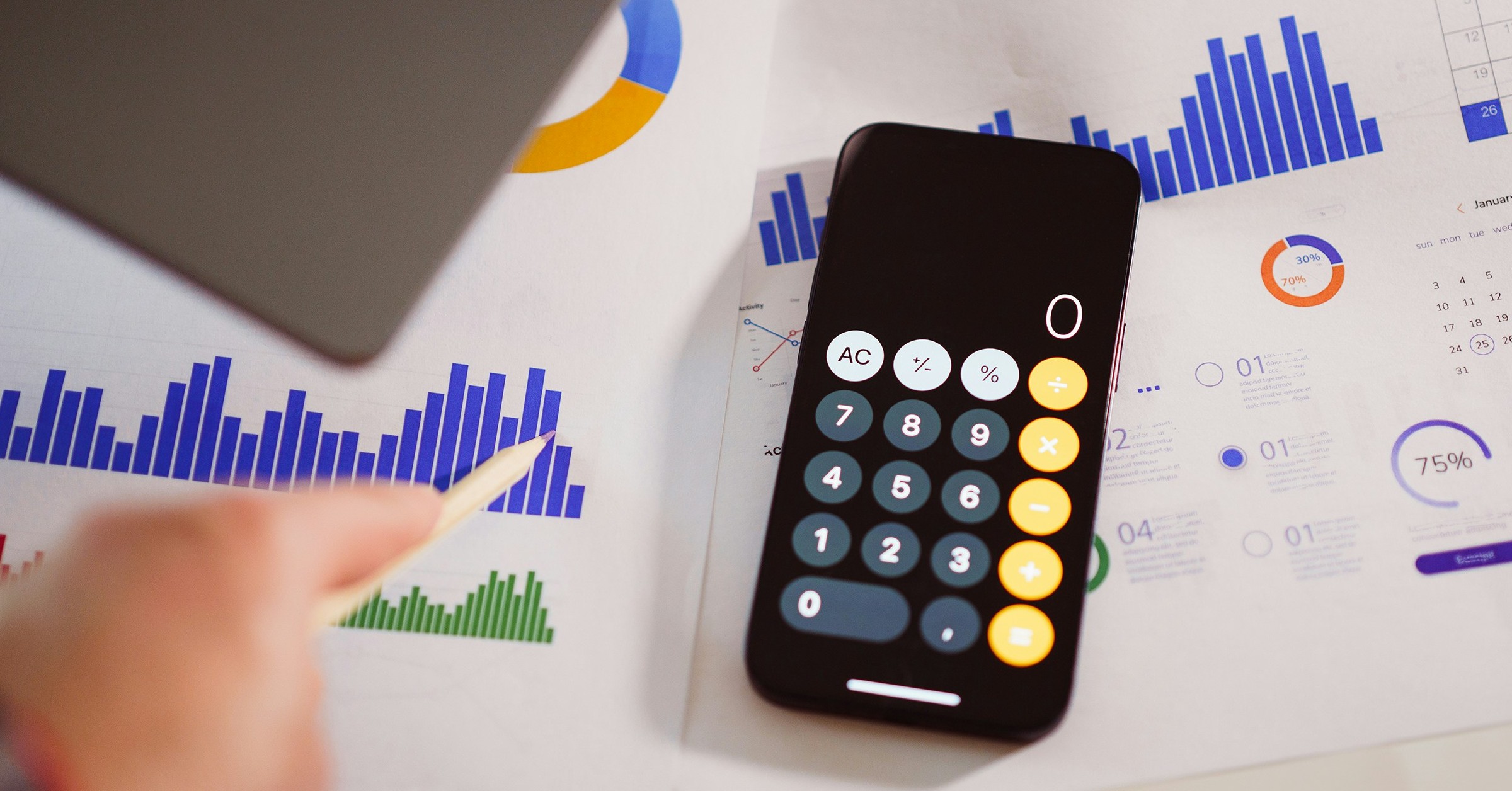 A smartphone with a calculator app open lies on paperwork with blue, green, and orange bar graphs and charts, while a person’s hand points at the data with a pencil—measuring impact beyond just a vanity metric.